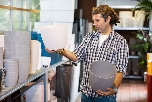 Schilderij op canvas Portrait of handsome man choosing pots for flowers and trees in gardening market