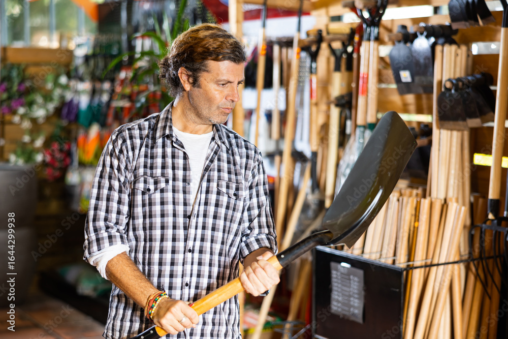 Fototapeta premium Caucasian farmer choosing shovel in garden shop