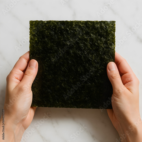 Hands holding square sheet of nori on marble surface  