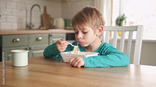 6 years old boy eats instant noodle from box. Child is eating spaghetti. Lunch time. A good appetite. Tasty children food. Close-up portrait. Carbs dinner. Fast food. Kid eating by himself with fork.