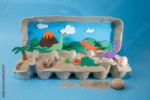 Bilde på lerret Handmade dinosaur diorama with paper cutouts, volcano, palm tree, eggs, sand in