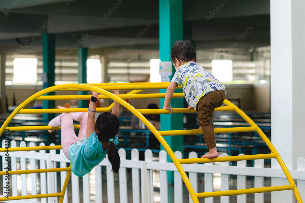 Naklejka premium Portrait of sister and brother playing on the playground together. Happy little child climbing on outdoor monkey bars. Kindergarten preschool. Children summer activities. Rear back view.