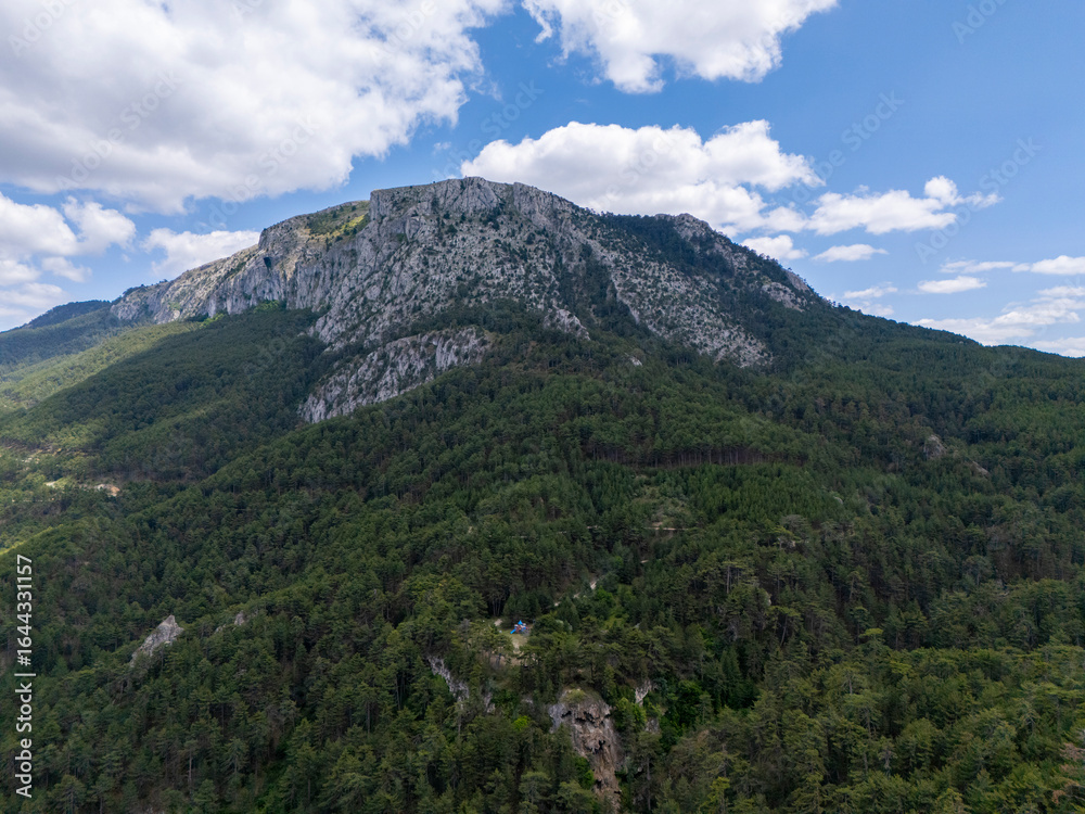 Fototapeta premium Aerial view of Sarıçalı Mountain in Nallıhan, Ankara National Park, showcasing lush green forests, rocky cliffs, and a beautiful sky with scattered clouds in a pristine natural environment.