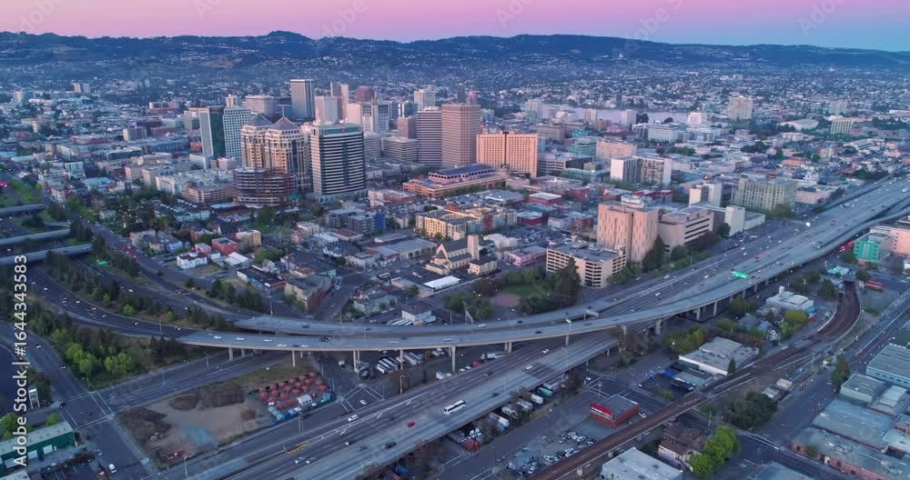 Aerial view of Oakland, California, USA, at sunrise. Cars travel on the highway below the city skyline, showcasing urban life and transportation. Aerial view of Oakland, California, USA, at sunrise. Cars travel on the highway below the city skyline, showcasing urban life and transportation.