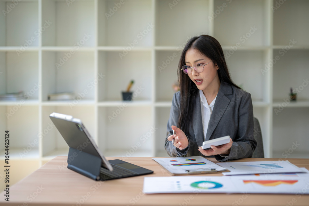 Businesswoman analyzing charts and holding calculator during video conference Businesswoman analyzing charts and holding calculator during video conference
