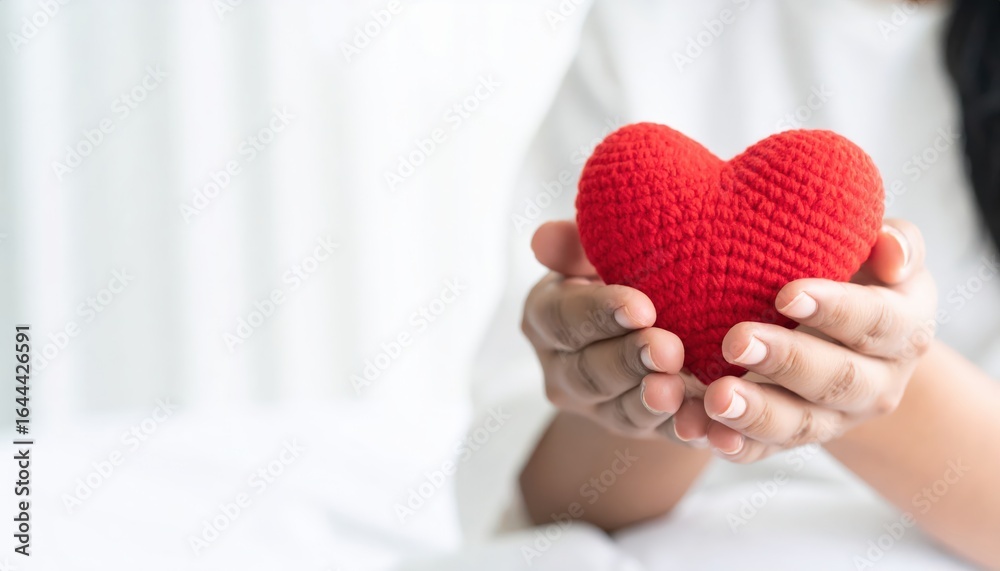 Fototapeta premium A person holds a red crocheted heart, symbolizing love and affection, against a softly blurred background.