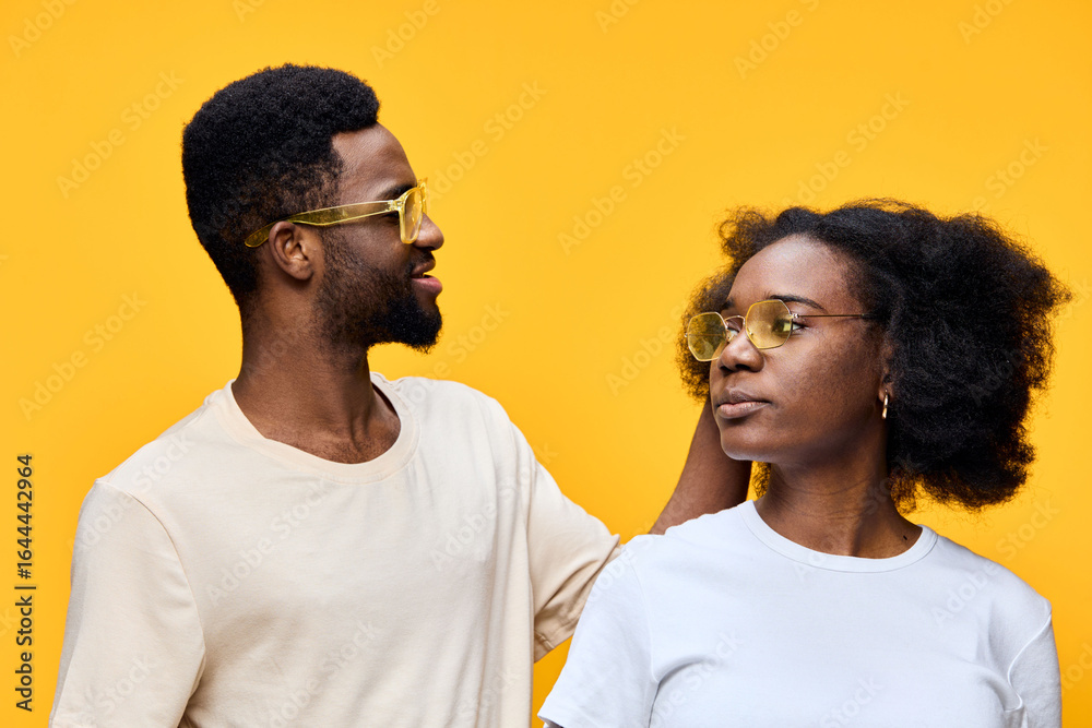 Fototapeta premium Happy young couple wearing sunglasses, with a vibrant yellow background, showcasing love and connection through playful emotions and stylish fashion