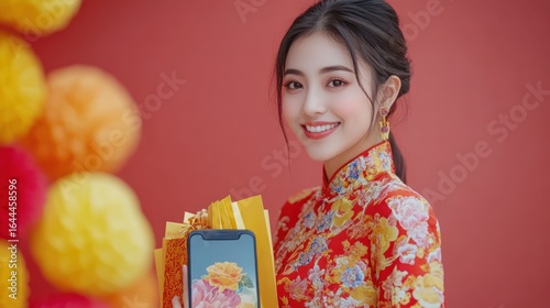A smiling woman in traditional attire holds gifts and a phone, posing against a red backdrop.
