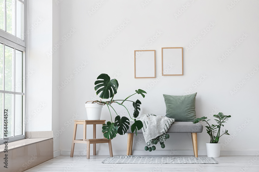 Fototapeta premium Interior of light room with soft bench, blank frames and plants