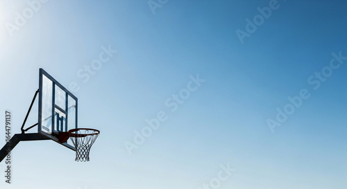 A basketball hoop with a transparent backboard silhouetted against a vast, clear blue sky.