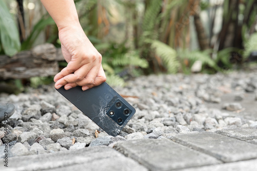 A person is holding a cell phone in their hand. The phone is black and has a cracked screen