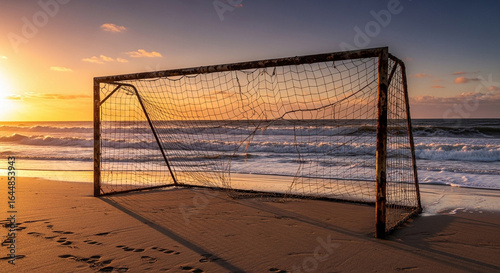A solitary, rusty soccer goal stands on a sandy beach as the sun sets over the ocean.