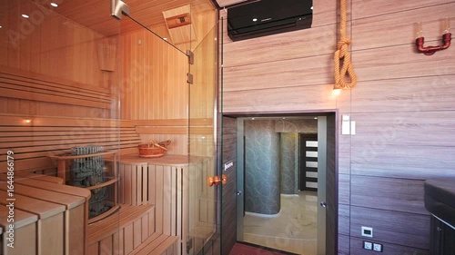 modern sauna features light wood interiors, glass doors, and a tiled shower area. A bucket and heating element sit inside.