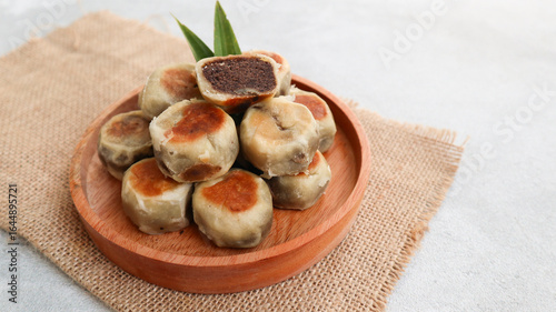 Bakpia Pathok filled with red beans or Kumbu Hitam served on wooden plate isolated on grey background. Original cake from Yogyakarta, Indonesia