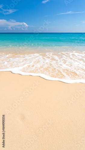 Fototapeta Naklejka Na Ścianę i Meble -  Tranquil beach scene; soft, white waves lap gently onto a smooth, pale sand shore under a vibrant blue sky