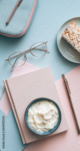 Flatlay of pastel stationery, eyewear, dessert, and cream in a bowl on a pink and blue background
