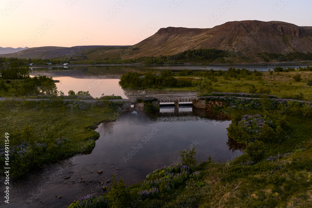 Obraz premium Small bridge crossing calm river at sunset in mosfellsbær, iceland