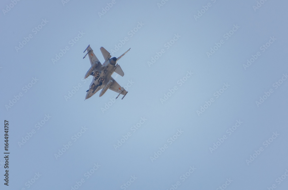 Fototapeta premium Fighter jet performing a steep banking maneuver in clear blue sky. Military fighter jet banking sharply during an aerial display against a bright blue sky.