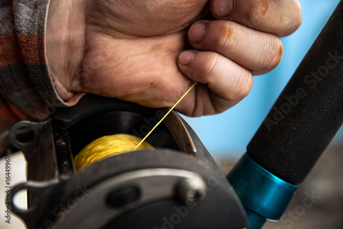 A fisherman holds yellow fishing line as he lets out slack from reel