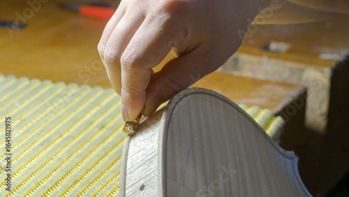 Obraz na plátně Close up of a luthier's hand working on a violin body, carefully placing a metal