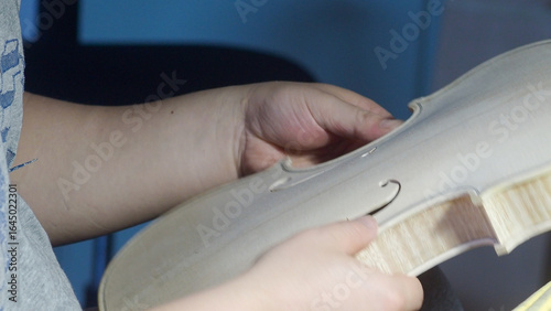 Fotografie Close up of luthier's hands holding and inspecting unfinished violin part, showc