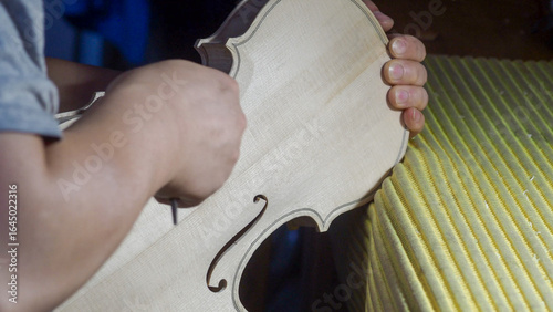 Fotografie Skilled luthier carving violin soundboard with precision gouge, revealing intric