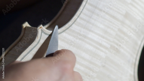 Fotografie Skilled craftsman carefully carving violin body with specialized knife, revealin
