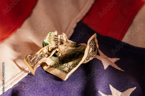 Crumpled United States one dollar bill lying on an American flag symbolizing economic challenges and financial struggles in the U.S. economy