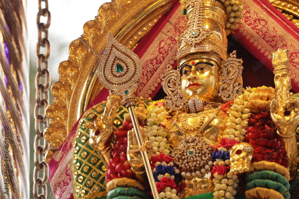 Fototapeta premium Golden Hindu deity statue adorned with traditional jewellery, vibrant garlands, and ceremonial attire during a festive religious procession in South India, symbolizing divinity and cultural heritage