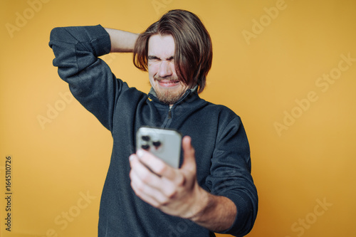 Photos portrait of young man expresses frustration while looking at his phone, with a v
