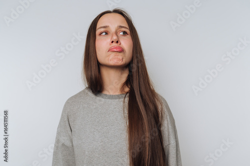 Foto portrait of young woman pouts with a sad expression on light background
