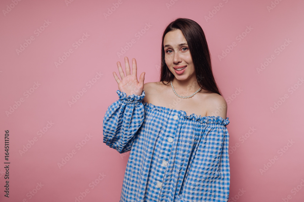 portrait of young woman waving enthusiastically while dressed in a stylish blue checkered shirt on pink background portrait of young woman waving enthusiastically while dressed in a stylish blue checkered shirt on pink background