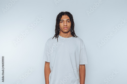 portrait of young man poses seriously, looking directly at the camera with a neutral expression on light background