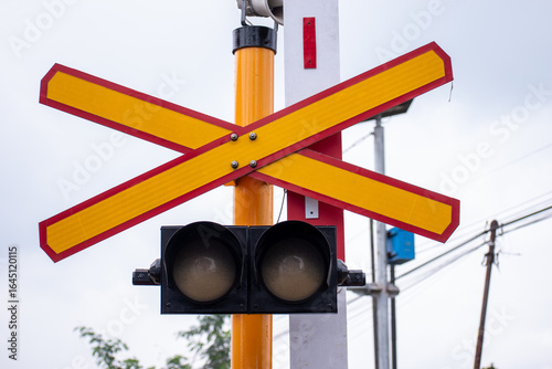 Close up view of a railway level crossing, marked by a prominent yellow and red X sign and a traffic light system.