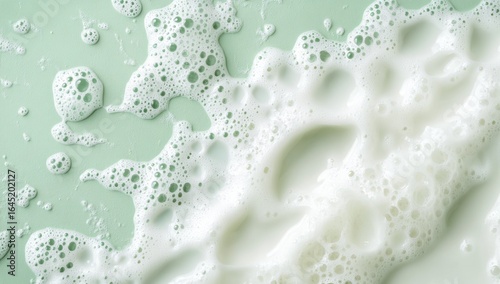 White foam and bubbles on a green background, flat lay. Top view. Milk or shampoo texture. Banner with copy space area for a design template.