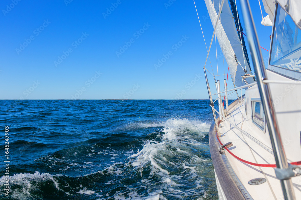 Obraz premium Luxury sailing yacht under genoa and mainsail cutting through waves of the Baltic Sea, Gulf of Finland. View from deck to bow, mast, and sails, emphasizing speed, motion, and yachting adventure