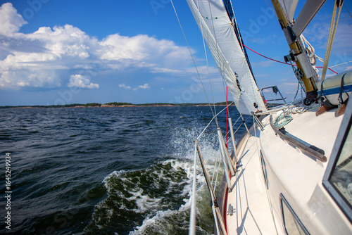 Luxury sailing yacht under genoa and mainsail cutting through waves of the Baltic Sea, Gulf of Finland. View from deck to bow, mast, and sails, emphasizing speed, motion, and yachting adventure