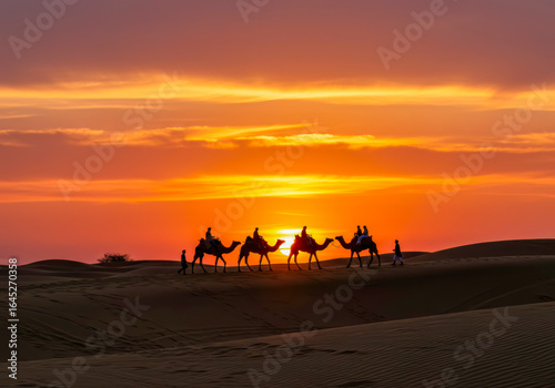 A majestic camel caravan and riders traverse sand dunes, silhouetted against a breathtaking vibrant sunset in the Indian desert.