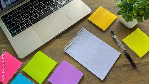 Laptop, colored sticky notes, notepad and pen on wooden table, concept of task planning and productive work in office or home.