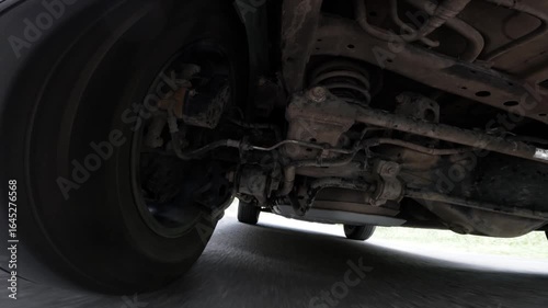 Camera on the underside of a car. The car is driving through the countryside. Focus on the car's suspension