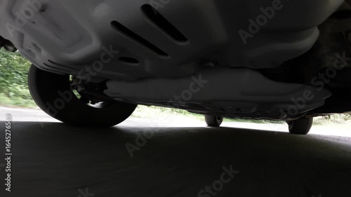 Camera on the underside of a car. The car is driving through the countryside. Focus on the car's suspension
