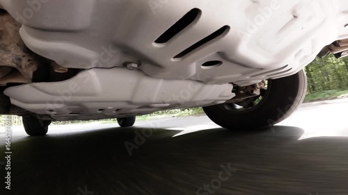 Camera on the underside of a car. The car is driving through the countryside. Focus on the car's suspension