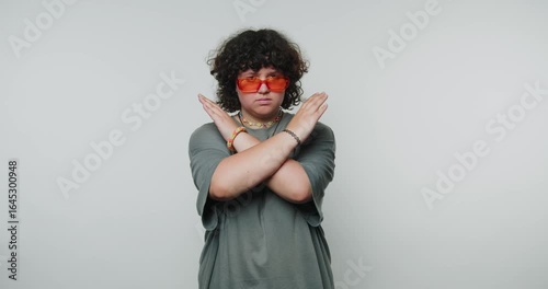 footage of young woman with curly hair wearing orange sunglasses is demonstrating a stop gesture on light background