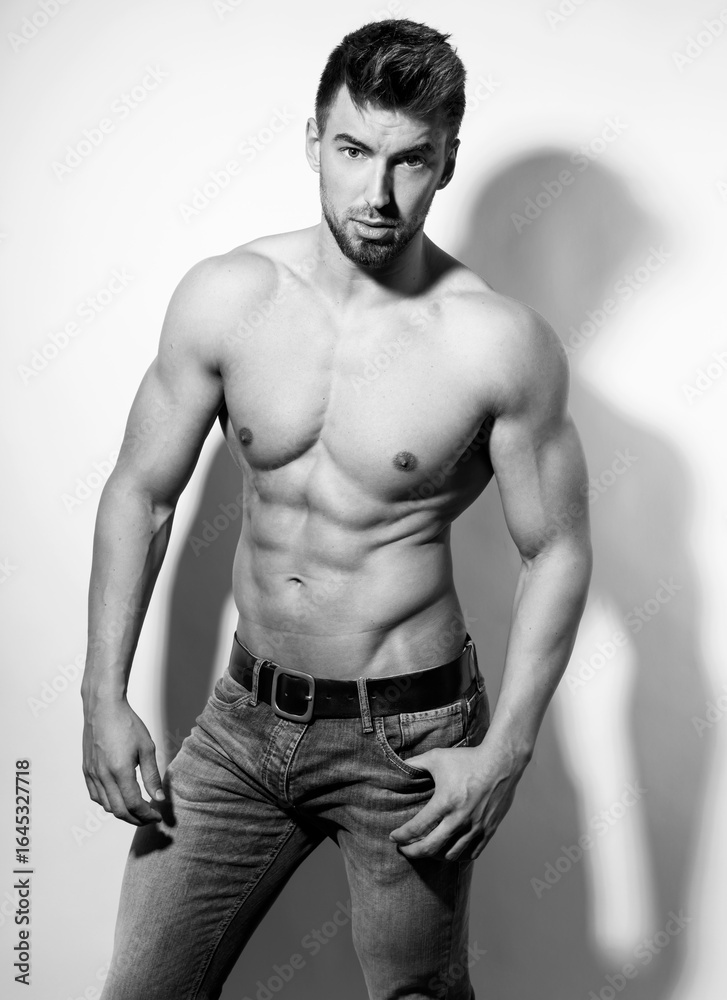 Naklejka premium Athletic and fit bodybuilder posing shirtless in jeans flexing muscles after workout showing off six-pack