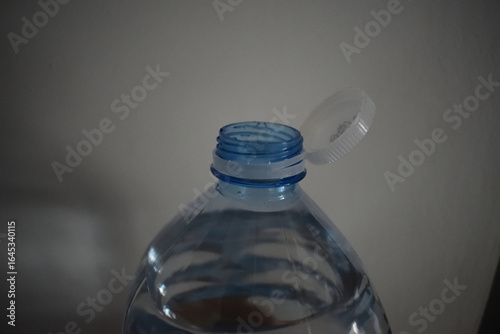A close-up of a plastic water bottle with a flip-open white cap and threaded neck, The bottle style and cap mechanism resemble those commonly found in European water bottle designs