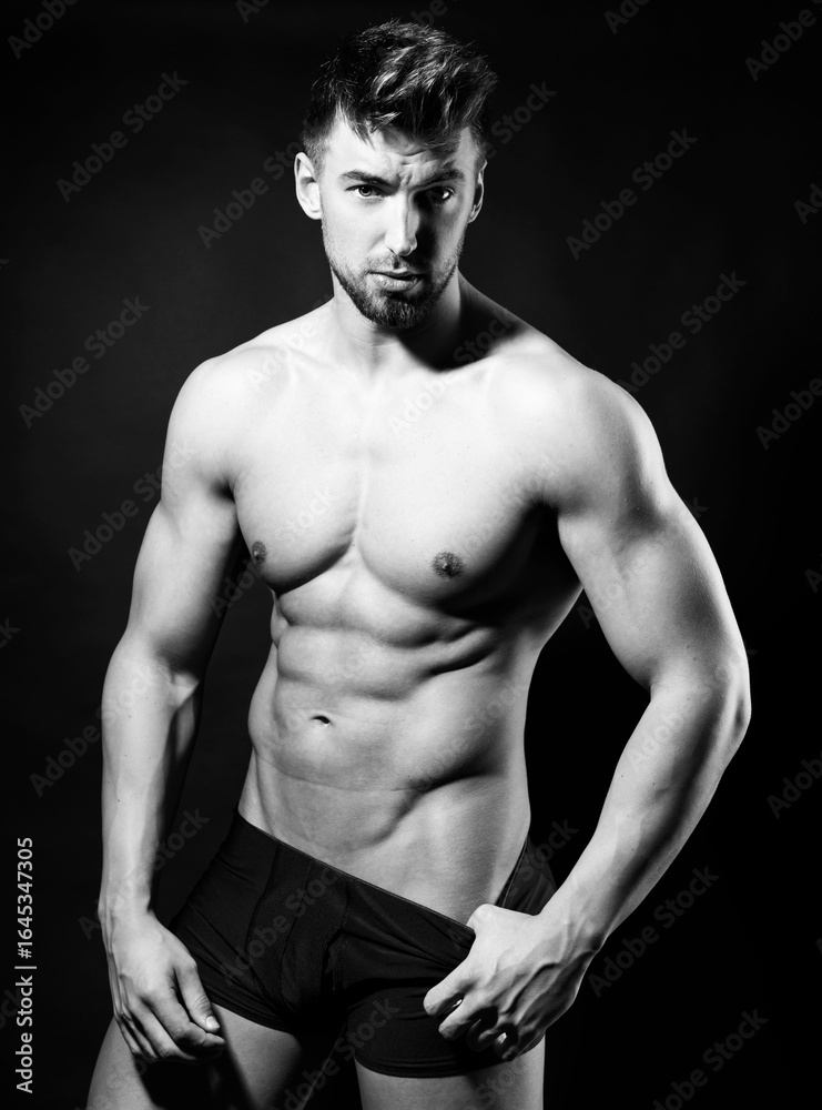Fototapeta premium Handsome young muscular bodybuilding man posing in underwear with visible six pack in black and white