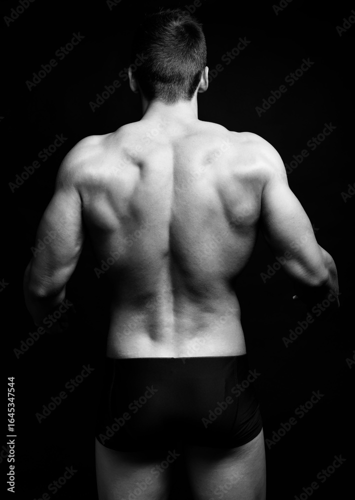 Fototapeta premium Handsome bodybuilding man posing shirtless on black background flexing muscles and six pack after a workout