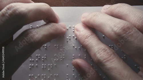 Visually impaired people use their fingertips to read Braille on paper. Text on the paper is a dummy Lorem ipsum text.
