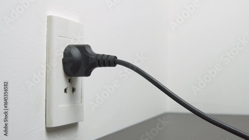 Female hand inserting a black electrical plug into outlet