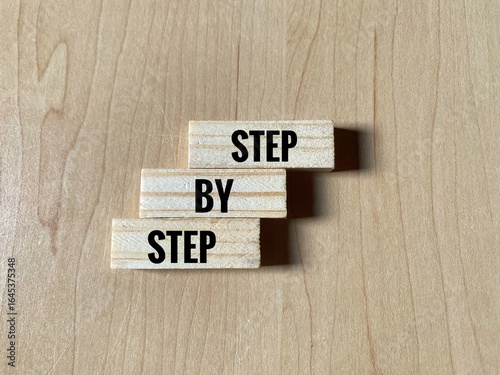 Three wooden blocks with Step By Step phrase over wooden surface. The concept of career or business growth.